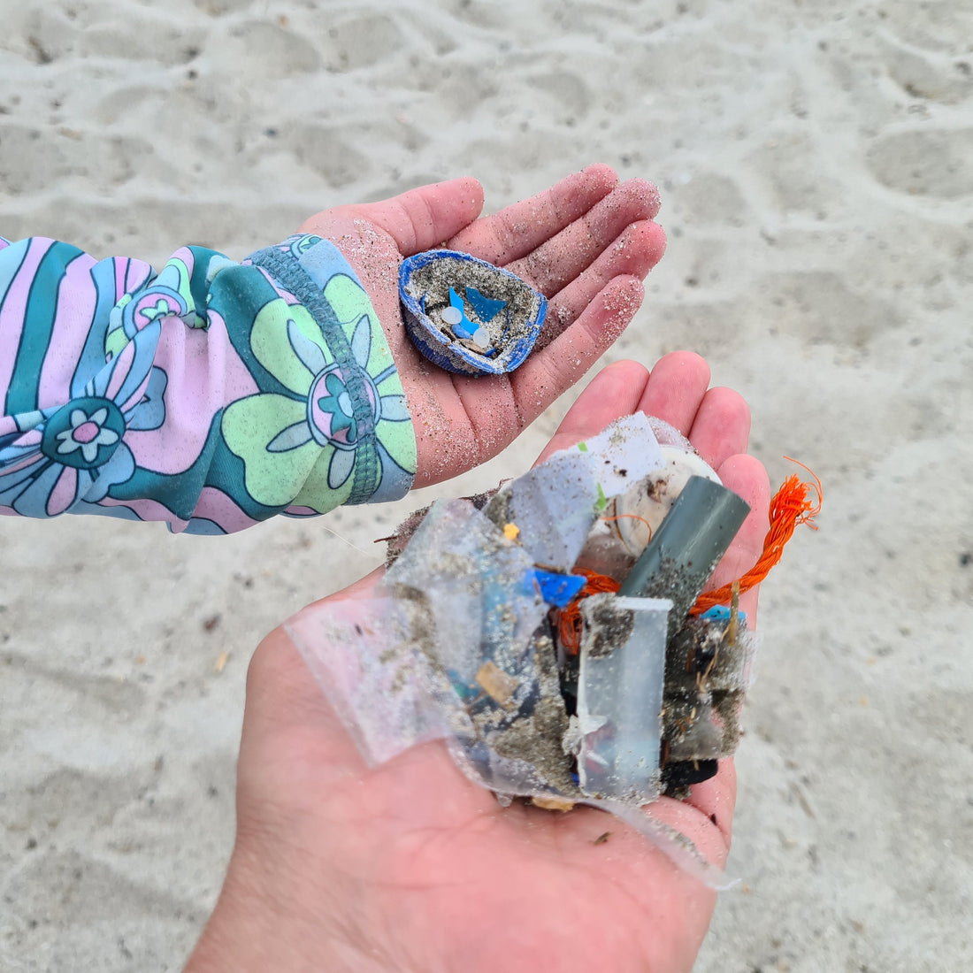 Hands holding small pieces of plastic found on a beach during a beach cleanup. 