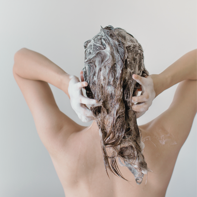 Person washing hair with shampoo, shown from the back.