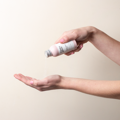 Hand pouring powder from a small bottle into another hand.